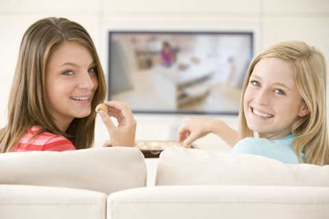 Two girls watching television and eating chocolate